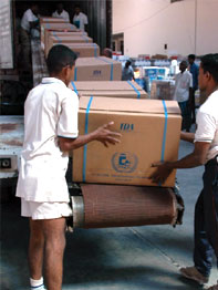 Workers loading boxes of supplies onto a conveyor belt inside a large warehouse