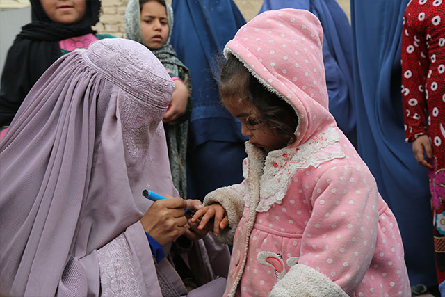 A girl looks on as her finger is marked after vaccination