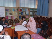 Des hommes et des femmes voilées sont réunis et discutent dans une salle de réunion-bibliothèque.