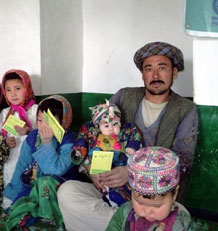 A man from Afghanistan proudly displays his vaccination card in the presence of his children