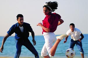 La photo nous montre des jeunes jouant au foot à la plage