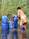 A man knee deep in flood water collects drinking water from a pump 